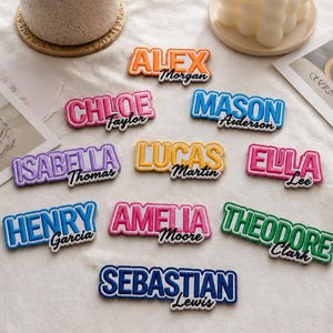 May include: A collection of embroidered name patches featuring various colors and fonts. Each patch displays a first name in large block letters with a smaller last name underneath, including names like Alex Morgan, Chloe Taylor, Mason Aiderson, Isabella Thomas, Lucas Martin, Ella Lee, Henry Garcia, Amelia Moore, Theodore Clark, and Sebastian Lewis.