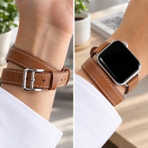 Peut inclure: Un bracelet de montre en cuir à double tour de couleur brun clair avec des surpiqûres blanches contrastantes. Le bracelet est doté d'une boucle en métal argenté et est fixé à une montre connectée rectangulaire à écran noir.