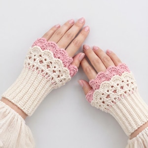 May include: A pair of fingerless gloves featuring a ribbed cream-colored cuff, a decorative cream-colored lace pattern above the cuff, and a scalloped pink crochet edge at the top. The gloves are crafted with intricate yarn work and layered textures.