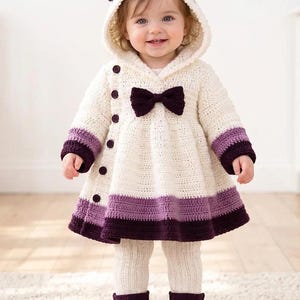 May include: A cream-colored crochet hooded coat featuring a dark purple bow at the neckline, dark purple cuffs, and a dark purple hem. The coat has a side-button closure with five dark purple buttons. It is paired with cream-colored knit leggings and dark purple boots.