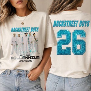 Pode incluir: Uma t-shirt de cor creme com um gráfico dos Backstreet Boys com o texto Into The Millennium Las Vegas na frente e o texto Backstreet Boys e o número 26 com um efeito de brilho azul na parte de trás da peça de vestuário.