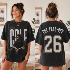 Può includere: Una t-shirt oversize grigio antracite con una grafica di J. Cole sul davanti insieme al testo 'J. Cole' e 'COLE'. Il retro della maglietta mostra il testo 'THE FALL-OFF' sopra il grande numero '26' in un carattere bianco dall'aspetto vissuto.