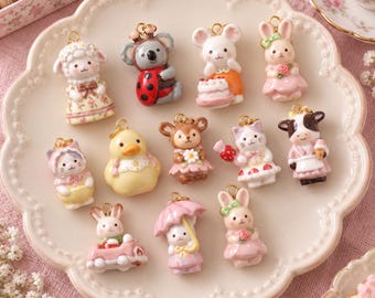 Könnte beinhalten: Eine Sammlung von zwölf kleinen, bunten Anhängern mit Tiermotiven, darunter ein Schaf, ein Koala im Marienkäferkostüm, eine Maus mit Torte, ein Hase, eine Katze, eine gelbe Ente, ein Reh, eine Katze mit Erdbeere, eine Kuh, ein Hase im Auto, ein Hase mit Regenschirm und ein Hase mit Rose.