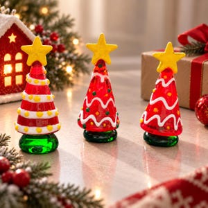 Puede incluir: Tres adornos cónicos de cristal para árbol de Navidad en rojo vibrante con bases verdes. Cada árbol presenta una estrella amarilla brillante en la punta y está decorado con líneas blancas onduladas y pequeños puntos amarillos, creando un conjunto festivo.