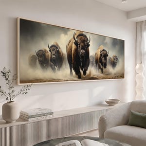 May include: A rectangular wall art print featuring a herd of brown bison running forward through a dusty, hazy landscape. The artwork is framed in a light-colored wood and depicts the animals with dark fur and prominent horns in a dynamic motion.