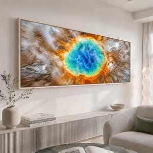 May include: A rectangular wall art print featuring an aerial view of a geothermal hot spring. The center is a vibrant, deep blue, surrounded by concentric rings of bright orange, yellow, and white mineral deposits, framed in a light wood border.