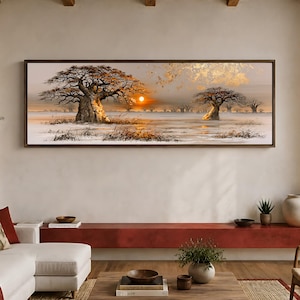 Op de afbeelding: Een breed rechthoekig ingelijst wandkunstwerk met een savannelandschap met twee prominente baobabbomen, droog gras en een heldere oranje zon aan de horizon. De scène heeft een warm kleurenpalet met gouden accenten en een zachte, wazige lucht.
