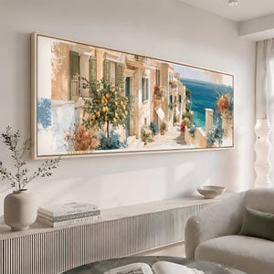 以下が含まれることがあります： ベージュの建物、緑の鎧戸、手前のレモンの木が描かれた地中海の沿岸の通りを写したパノラマのウォールアートプリント。鮮やかな青い海、カラフルな花のアクセント、明るい色のフレームで構成されています。