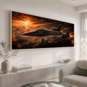 Op de afbeelding: Een rechthoekige wandkunstprint met een zwart SR-71 Blackbird-vliegtuig dat bij zonsondergang door een levendige oranje en donkere, met wolken gevulde lucht vliegt. Het vliegtuig toont de tekst U.S. AIR FORCE en heeft een licht houten frame.