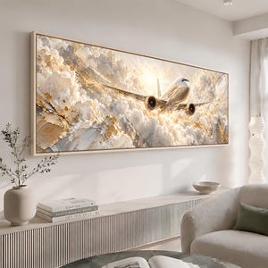 Può includere: Una stampa artistica da parete rettangolare che raffigura un aereo commerciale in volo attraverso un cielo denso di nuvole bianche e dorate. L'opera presenta pennellate spesse in stile impasto nei toni del crema, bianco e oro metallizzato, con il sole che brilla intensamente dietro il velivolo.