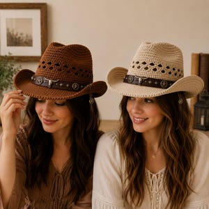 May include: Two cowboy hats, one in brown and one in beige, featuring a crocheted texture with a diamond-patterned crown. Each hat includes a dark brown band adorned with a central silver-toned bull skull emblem and circular star-shaped studs.