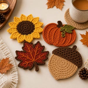 May include: A set of four crocheted coasters featuring autumn-themed designs: a yellow sunflower with a brown center, an orange pumpkin with a green leaf, a red maple leaf, and a tan acorn with a dark brown cap, all crafted with yarn.