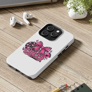 Op de afbeelding: Een witte smartphonehoes met een grafisch ontwerp van een roze cheer-strik met luipaardprint, een megafoon en pompons, met het woord CHEER in dikke roze letters en kleine ster- en hartaccenten op een witte achtergrond.