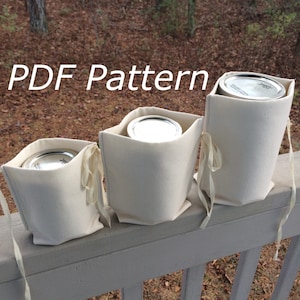 Puede incluir: Tres bolsas de tela blanca con cierre de cordón, cada una contiene un frasco de metal de diferente tamaño. Las bolsas están alineadas en una barandilla de madera blanca. El texto "PDF Pattern" está escrito en letras blancas sobre un fondo marrón en la parte superior de la imagen.