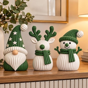 Op de afbeelding: Een set van drie decoratieve beeldjes bestaande uit een kabouter met een hoge groene muts met witte sterren, een rendier met groen gewei en een sneeuwpop met een groene muts en sjaal. Elk figuur heeft een geribbelde textuur en wit-groene kleur.