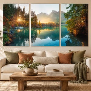 May include: A triptych wall art set featuring a landscape photograph of a turquoise lake surrounded by dense pine forests and distant mountains at sunrise. The three panels display a continuous scene with reflections of the trees and peaks in the water.
