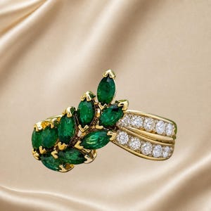 May include: A gold ring featuring a cluster of marquise-cut green gemstones arranged in a leaf-like pattern, accented by two parallel rows of round brilliant-cut clear stones set along the band, creating a detailed and ornate jewelry piece.