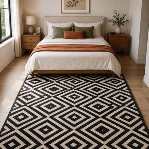 May include: A rectangular area rug featuring a repeating geometric pattern of black and cream-coloured diamonds. The rug is positioned on a light-coloured wooden floor in front of a bed with white bedding, olive green pillows, and a rust-coloured throw blanket.