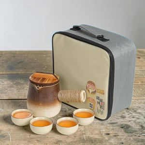 May include: A ceramic teapot with a brown and cream gradient finish, a wooden lid, and a rope-wrapped side handle, accompanied by four small matching tea cups and a grey and beige fabric carrying case with a printed graphic and Chinese text.