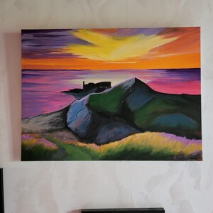 Puede incluir: Un cuadro rectangular sobre lienzo que representa un paisaje costero al atardecer. El cielo muestra tonos amarillos y naranjas vibrantes sobre un mar de color púrpura y rosa intenso. Un promontorio rocoso oscuro se adentra en el agua.