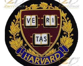 May include: A circular embroidered patch featuring a maroon shield with three white open books bearing the black text VERI TAS. The shield is surrounded by gold wheat stalks and a blue ribbon at the bottom with the gold embroidered text HARVARD.