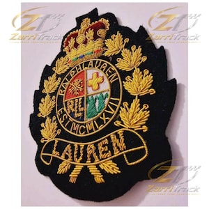 May include: A black embroidered patch featuring a gold crown at the top and a central circular crest with four quadrants. The text RALPH LAUREN EST MCMLXVII is stitched around the circle, with LAUREN on a banner below, surrounded by gold leaves.