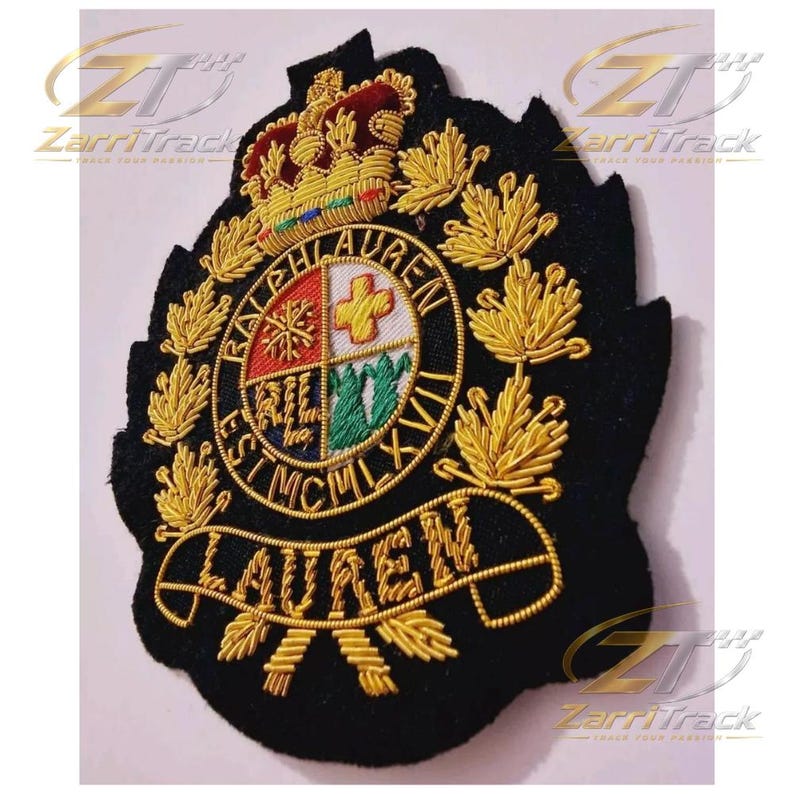 May include: A black embroidered patch featuring a gold crown at the top and a central circular crest with four quadrants. The text RALPH LAUREN EST MCMLXVII is stitched around the circle, with LAUREN on a banner below, surrounded by gold leaves.