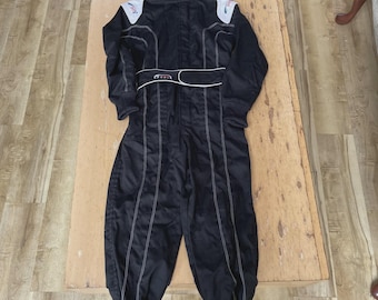 May include: A black racing suit featuring a high collar, long sleeves, and white shoulder panels with red and green accents. The garment includes a central waist belt with a white trim and white contrast stitching running vertically down the legs.