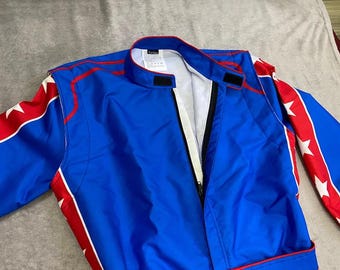 May include: A blue racing jacket featuring a high collar with a hook-and-loop closure, a front zip, and red side panels on the sleeves decorated with white stars. The jacket has a white inner lining and red piping accents along the shoulders.