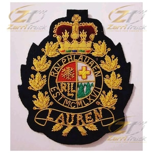 May include: A black embroidered patch featuring a gold crown at the top and a central circular crest divided into four quadrants with symbols. The text RALPH LAUREN EST MCMLXVII is stitched around the circle, with LAUREN on a banner below.