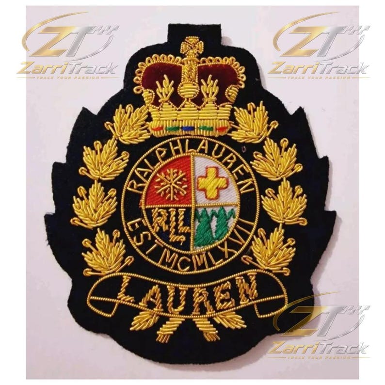 May include: A black embroidered patch featuring a gold crown at the top and a central circular crest divided into four quadrants with symbols. The text RALPH LAUREN EST MCMLXVII is stitched around the circle, with LAUREN on a banner below.