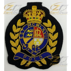 May include: A black embroidered patch featuring a gold crown at the top, surrounded by gold laurel leaves. A central blue circular border contains the text MCMLXVIII and POLO. The shield displays gold lions, a letter R, and fleur-de-lis symbols.