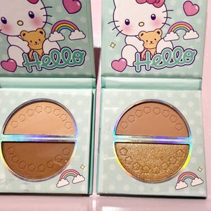 Puede incluir: Dos paletas de maquillaje cuadradas con Hello Kitty, un osito de peluche y arcoíris sobre un fondo azul claro de lunares. Cada paleta contiene dos compartimentos semicirculares con pequeñas flores en relieve, en acabados mate y brillantes.
