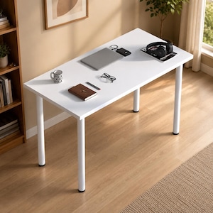 May include: A rectangular white desk with four cylindrical white legs. The surface holds a gray laptop, a black external hard drive, black headphones, a patterned mug, a brown notebook, a black pen, and black-rimmed eyeglasses.