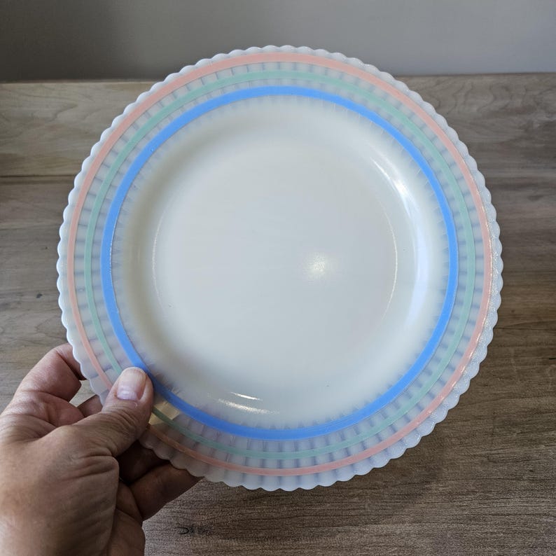 May include: A white plate with a scalloped edge and pastel blue, green, and pink bands. The plate has a simple, elegant design, suitable for serving food. The plate is made of a durable material.
