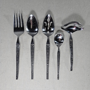 May include: Set of five silver-toned serving utensils with floral patterned handles. The set includes a fork, a large spoon, a slotted spoon, a small spoon, and a gravy ladle.