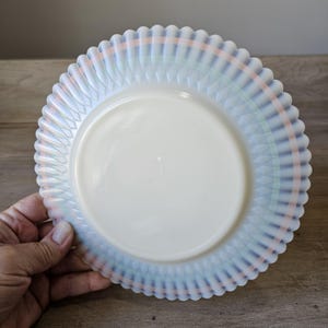 May include: A vintage white glass plate with a scalloped edge. The plate features a pastel plaid design in shades of blue, green, and peach. The plate is round and has a diameter of approximately 9 inches.