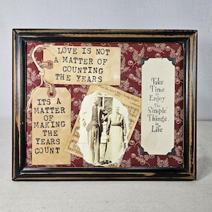 Pode incluir: Obra de arte emoldurada com uma moldura preta desgastada. A obra apresenta um fundo bordô com padrões florais brancos. Inclui etiquetas vintage com texto, uma foto em tons sépia e as frases "O amor não é uma questão de contar os anos" e "Tire um tempo para aproveitar as coisas simples da vida".