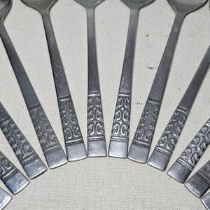 May include: A set of ten silver spoons with an ornate design. The spoons are arranged in a fan shape, with the handles pointing outwards.