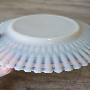 May include: A white, opalescent glass bowl with a scalloped edge. The bowl has a diamond pattern on the side and a flat, circular base. The rim has a subtle rainbow iridescence.