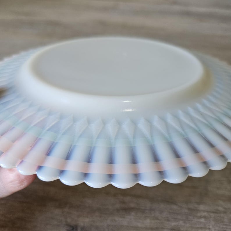 May include: A white, opalescent glass bowl with a scalloped edge. The bowl has a diamond pattern on the side and a flat, circular base. The rim has a subtle rainbow iridescence.