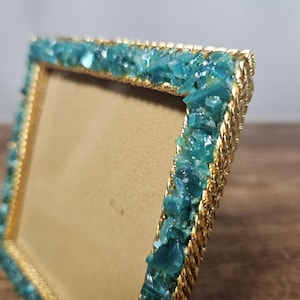 May include: Gold picture frame with a turquoise blue border made of small glass pieces.