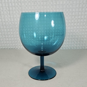 May include: A teal-colored, stemmed glass with a rounded bowl and a circular base. The glass is made of a transparent material, allowing light to pass through. The stem and base are the same color as the bowl.