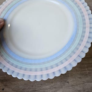 May include: A white plate with pastel blue, green, and pink stripes and a scalloped edge. The plate has a smooth, glossy surface and a simple, elegant design. The plate is likely for serving food.