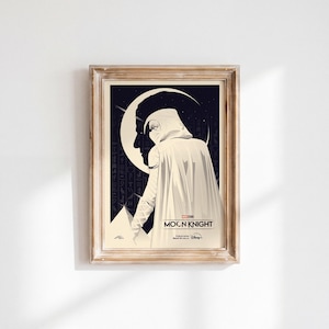 Op de afbeelding: Een ingelijste poster met een grafische illustratie van een figuur met een kap in een witte mantel tegen een donkere achtergrond met een halve maan en Egyptische hiërogliefen. De tekst luidt MOON KNIGHT, Marvel Studios en Disney Plus.