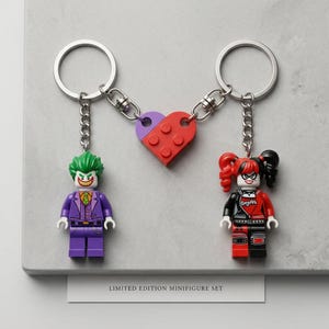 Pode incluir: Dois porta-chaves de metal com minifiguras de plástico de uma personagem de cabelo verde com fato roxo e uma personagem vermelha e preta com tranças. Estão ligados por uma peça de plástico em forma de coração vermelha e roxa. Texto: LIMITED EDITION MINIFIGURE SET.