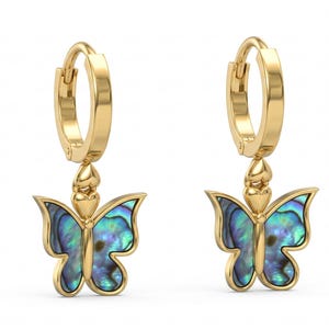 May include: A pair of gold hoop earrings featuring dangling butterfly charms. Each butterfly has a polished gold frame and iridescent blue and green abalone shell inlay. The charms are attached to the hoops by a small gold heart-shaped connector.
