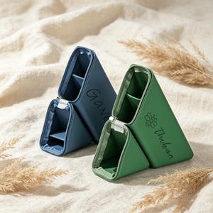 May include: Two triangular pencil cases, one blue and one green, featuring internal dividers and zipper closures. The blue case is personalized with the name "Gavin," while the green case features a bee icon and the name "Thuhan" printed on the side.