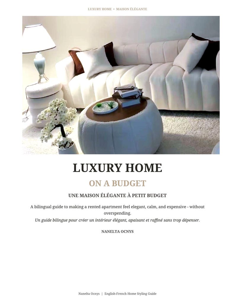 May include: A book cover titled LUXURY HOME ON A BUDGET, UNE MAISON &Eacute;L&Eacute;GANTE &Agrave; PETIT BUDGET by Nanelta Ocnys. The cover features a photograph of a white channel-tufted sofa, a round white ottoman, a table lamp, and a small potted white floral plant.