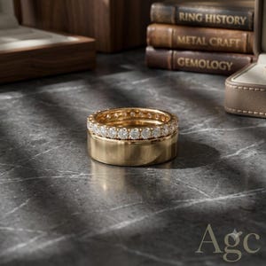 May include: A gold ring set consisting of a wide, polished gold band stacked beneath a thinner gold eternity band featuring a continuous row of round, clear, faceted stones set along the entire circumference of the metal band.